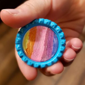 Round pin with scalloped bright blue ring and edge-to-edge hand-drawn rainbow colors