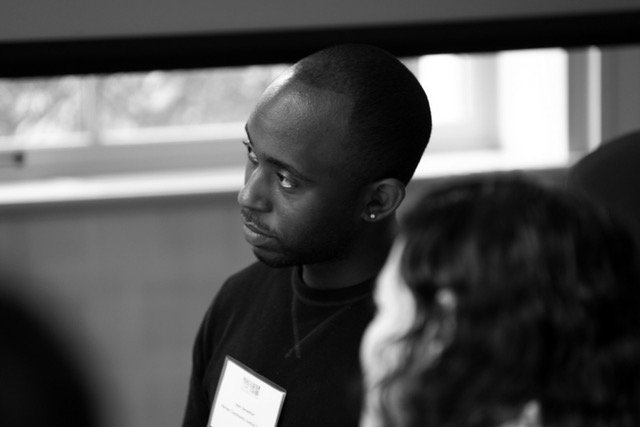 Person in black sweater with name tag looking intently out of frame